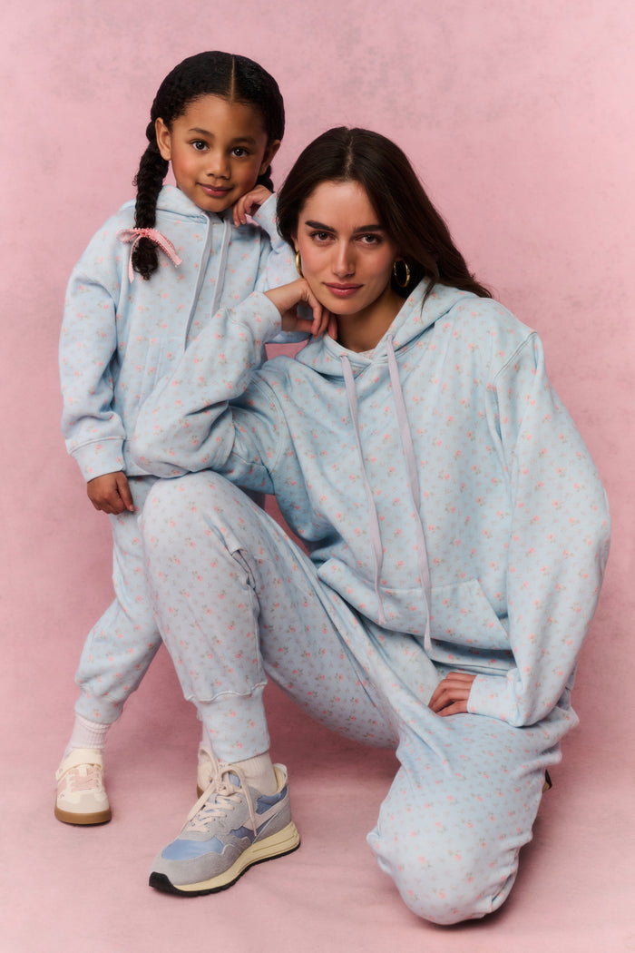 Two people wearing matching light blue sweat sets on a pink background