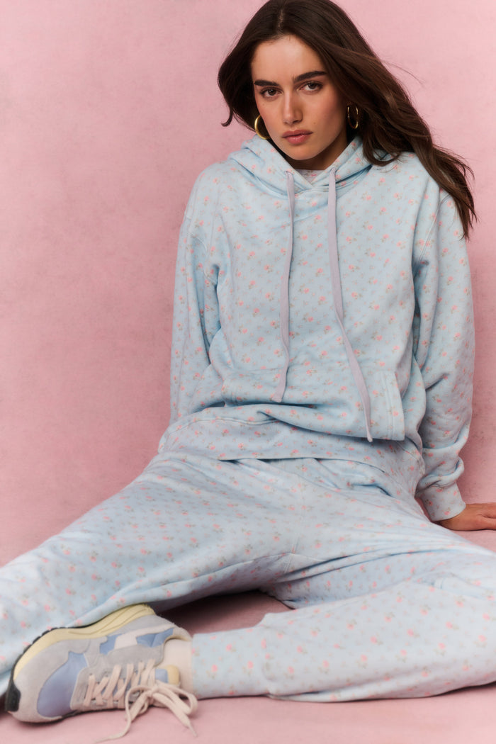 Woman wearing a light blue floral hoodie and pants sitting on a pink background