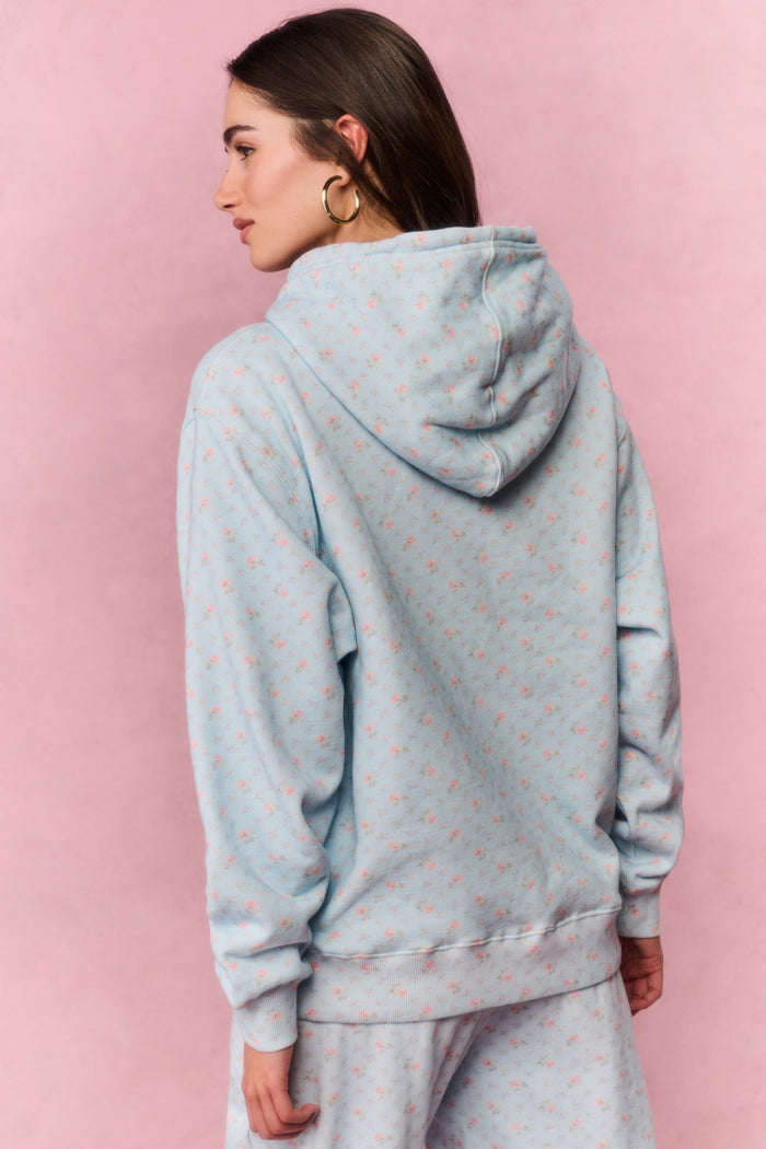 Woman wearing a light blue floral hoodie and pants sitting on a pink background