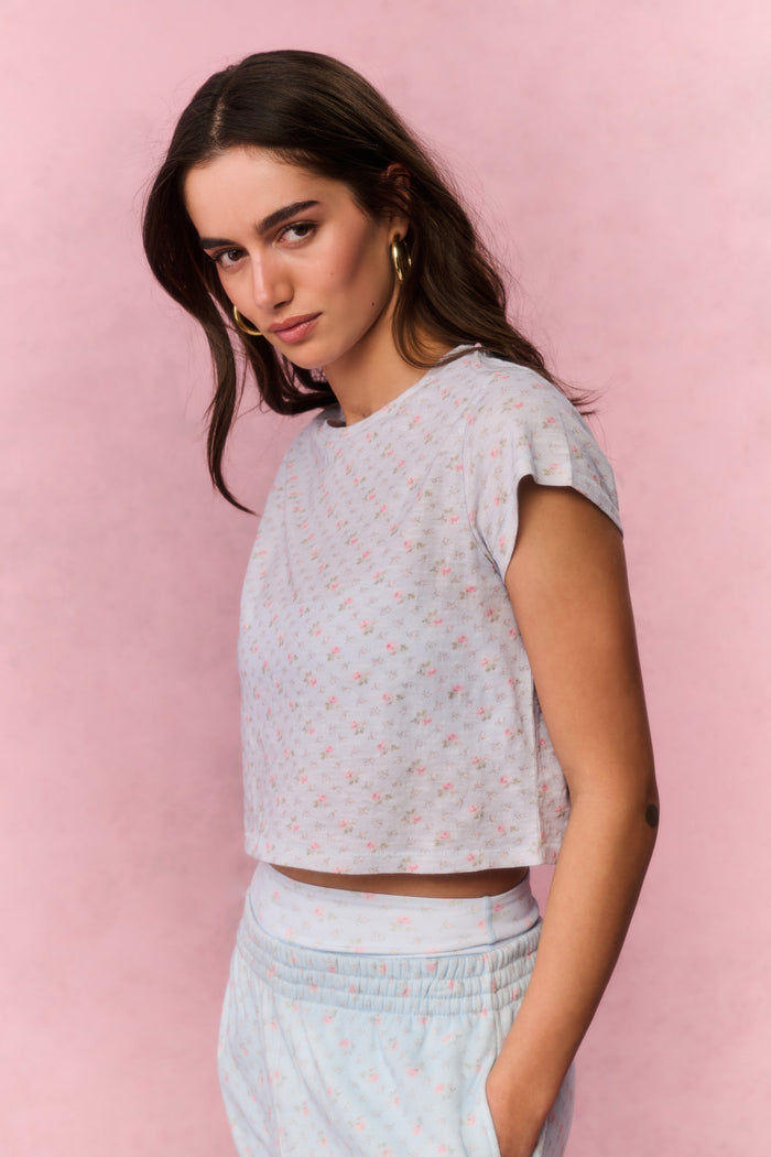 Woman wearing a light blue top and pants with a subtle pattern against a pink background