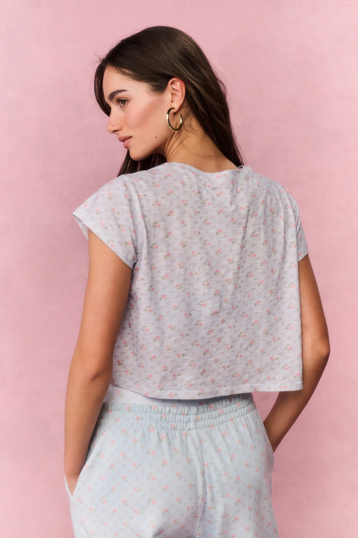Woman wearing a light blue floral top and pants against a pink background