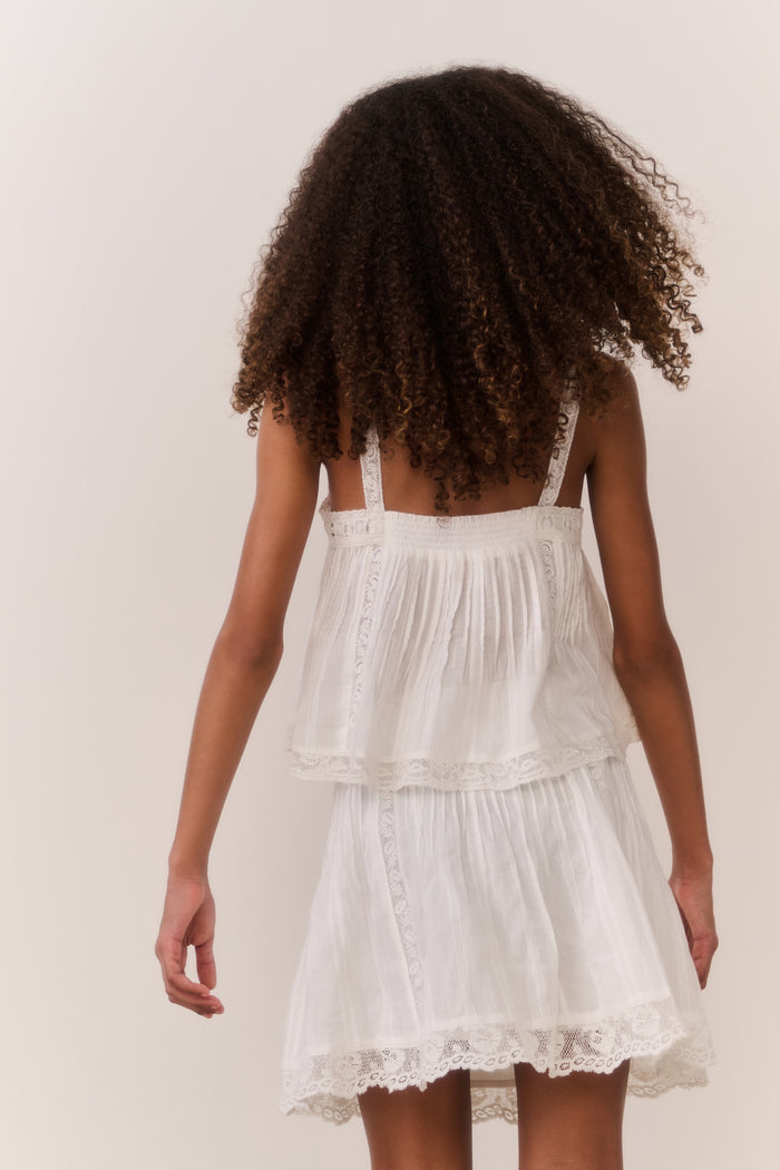 Tween girl wearing white lace trim camisole and matching skirt against white background