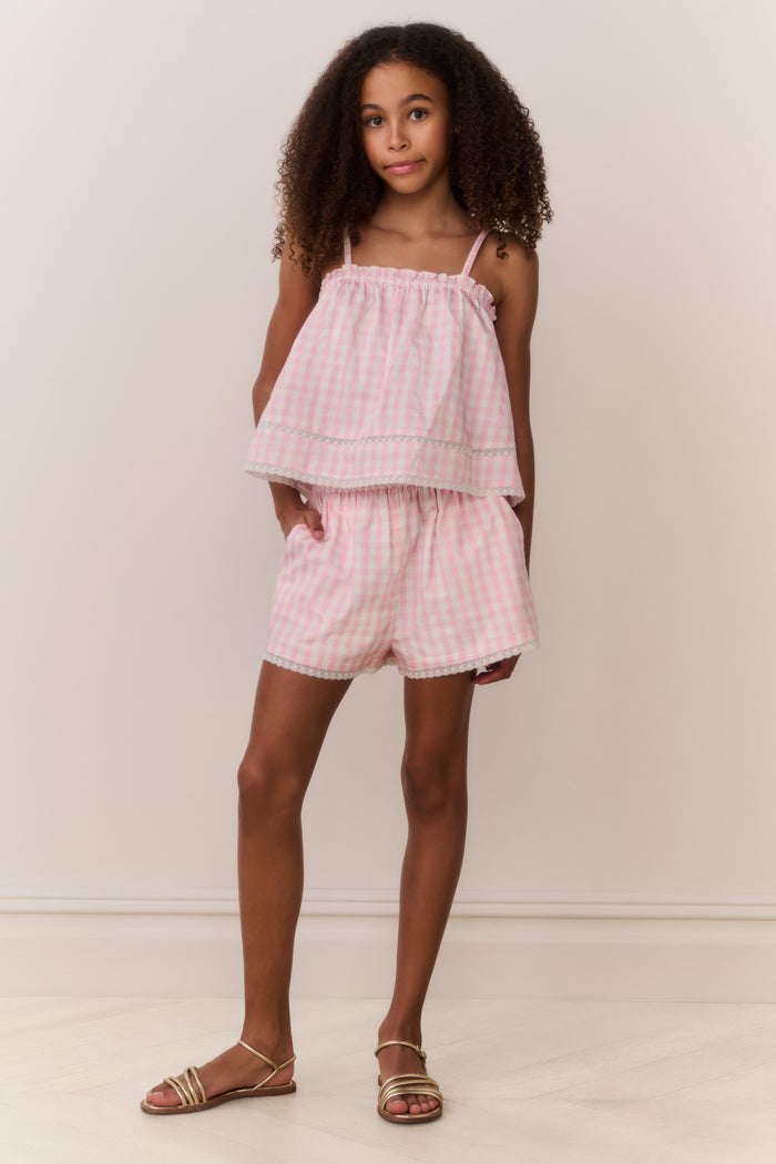Young girl wearing a matching pink checkered sleeveless and shorts outfit against a plain background