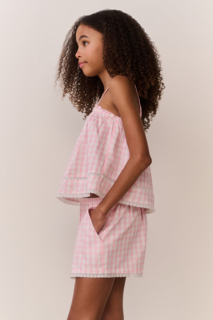 Young girl wearing a matching pink checkered sleeveless and shorts outfit against a plain background