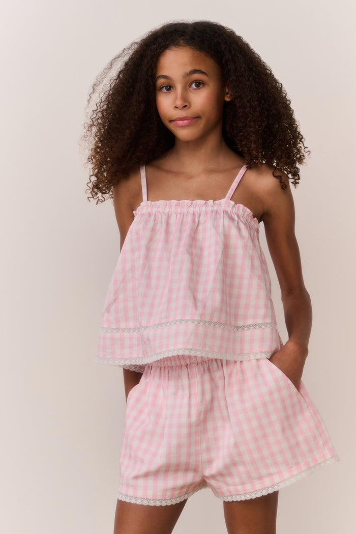 Tween wearing a pink checkered outfit against a plain background