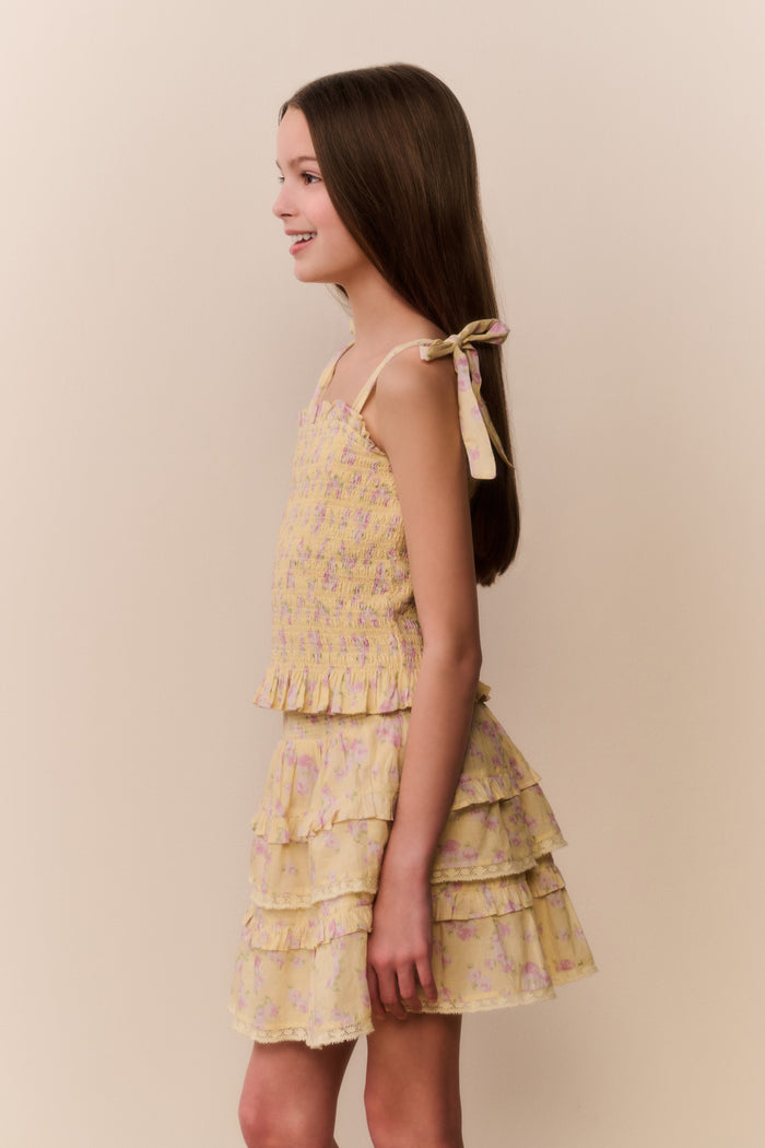 Young girl wearing a yellow floral top and matching skirt with ruffled layers on a beige background