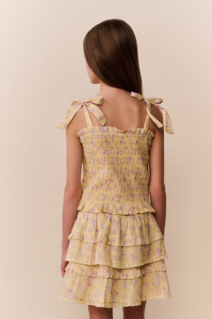 Young girl wearing a yellow floral top and matching skirt with ruffled layers on a beige background