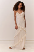 Tween girl wearing a flowing white sleeveless dress with ruffles on a plain background