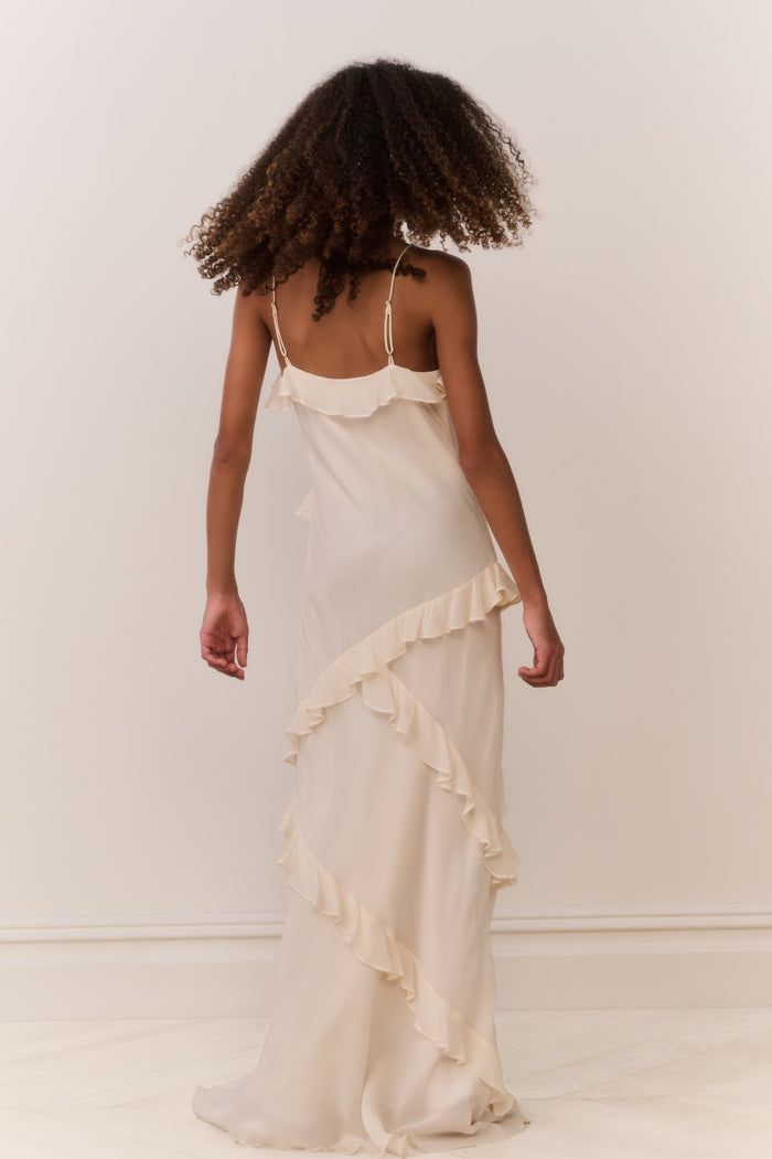 Tween girl wearing a flowing white sleeveless dress with ruffles on a plain background