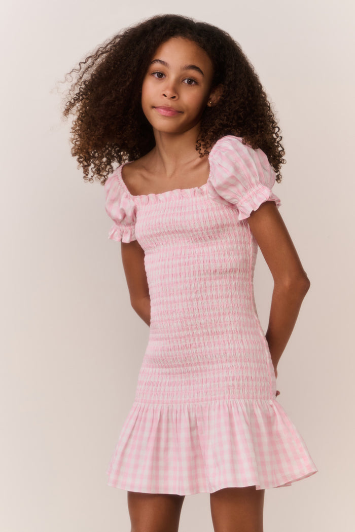 Girl wearing a pink checkered dress with a plain background