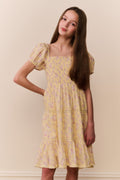 Young girl wearing a yellow floral dress against a plain background