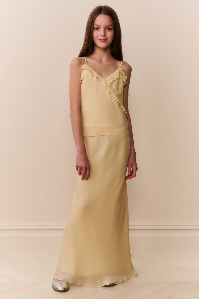 Girl wearing a light yellow sleeveless ruffle detail top and matching long skirt against a beige background