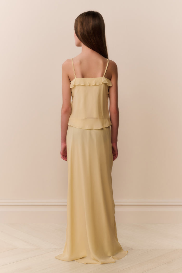 Girl wearing a light yellow sleeveless ruffle detail top and matching long skirt against a beige background