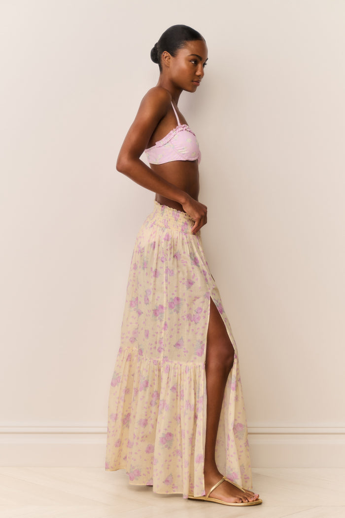 Woman wearing a pink bikini top and floral skirt against a plain background