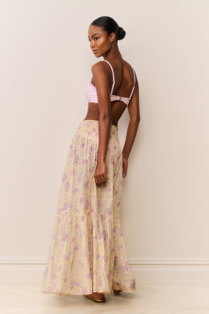 Woman wearing a pink bikini top and floral skirt against a plain background