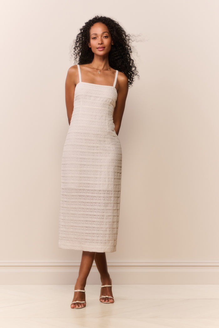 Woman wearing a white textured sleeveless dress against a plain background