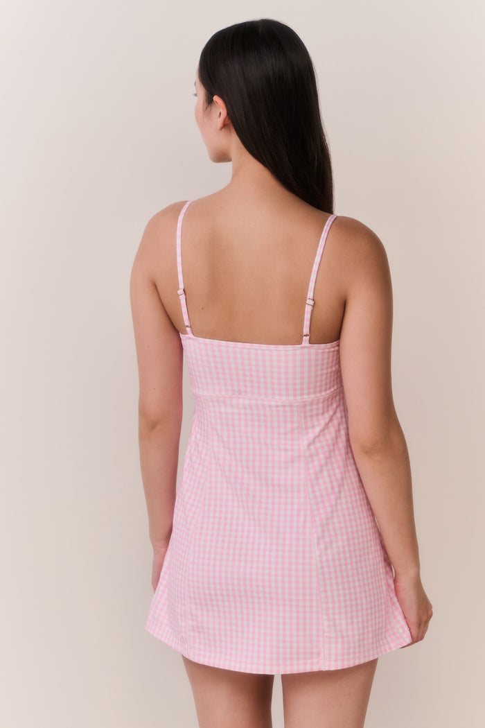 Woman wearing a pink checkered dress with thin straps on a beige background