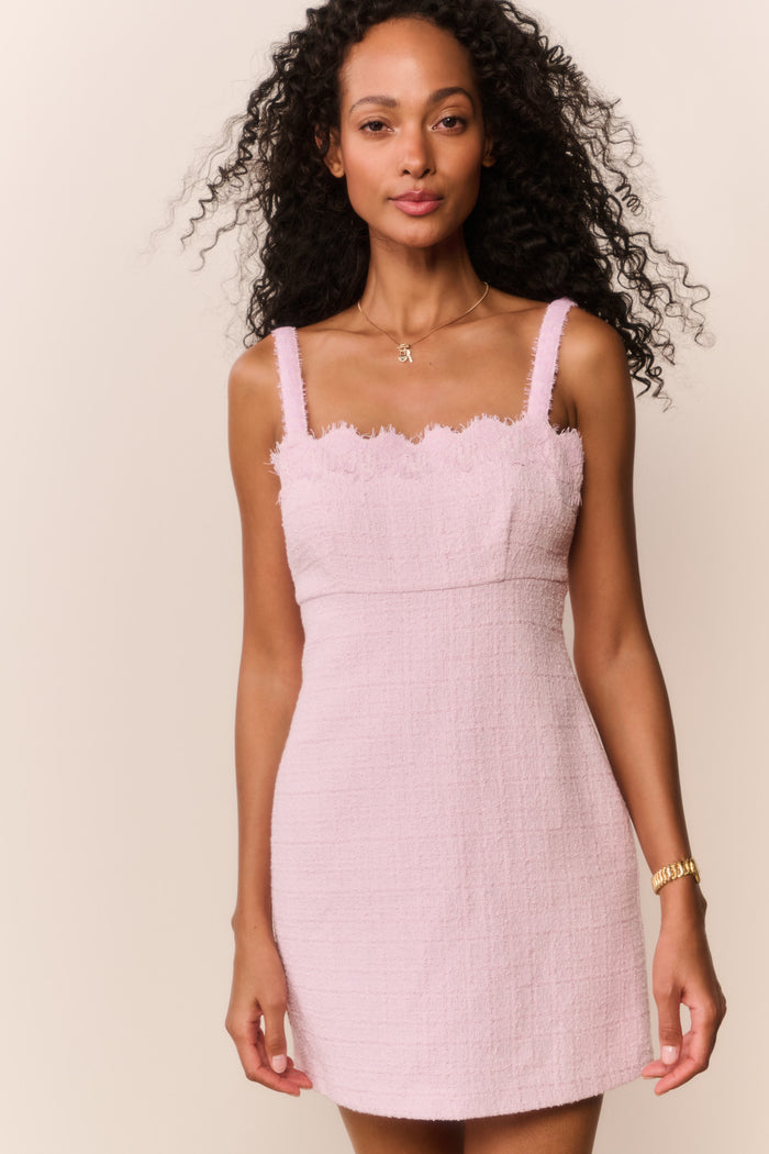 Woman wearing a pink dress with thin straps and scalloped neckline against a beige background