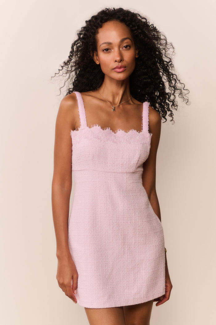 Woman wearing a pink dress with thin straps and scalloped neckline against a beige background