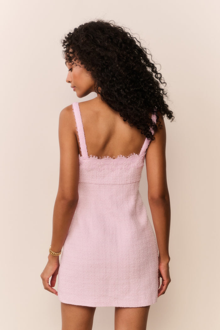 Woman wearing a pink dress with thin straps and scalloped neckline against a beige background