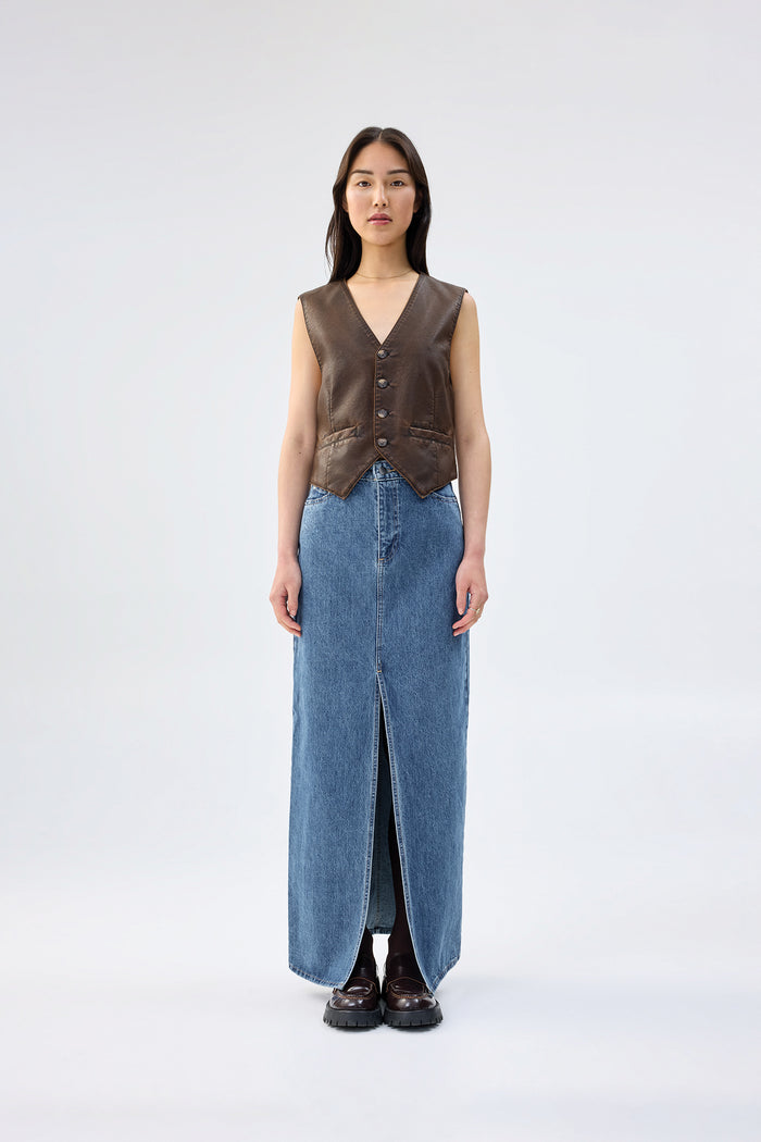 Brown vegan leather vest with button-front closure and V-neckline, worn over a blue denim maxi skirt, front view