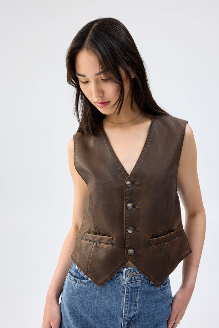 Close-up of a model wearing a brown faux leather vest with button-front closure and V-neckline, looking down