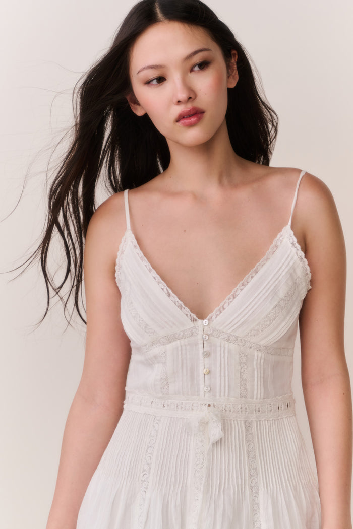 Woman wearing a white lace sleeveless dress against a plain background